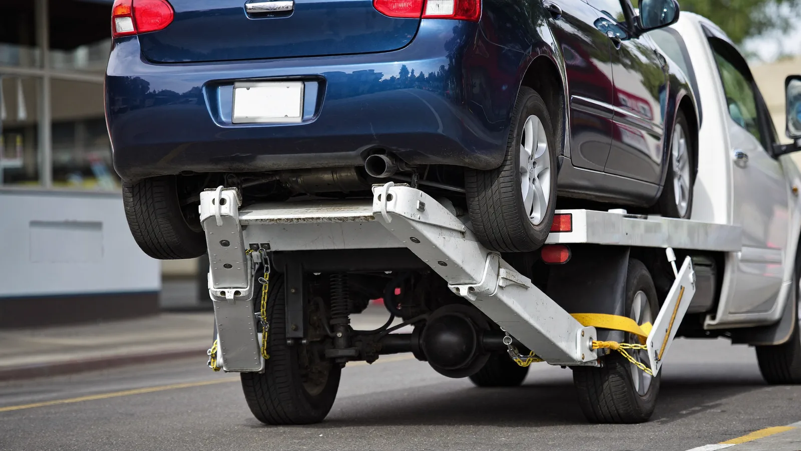 Wheel-lift tow truck yoke holding the rear wheels of a small car off the road